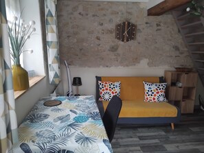 Une pièce confortable avec un lit, un canapé, une horloge murale et une étagère en bois.