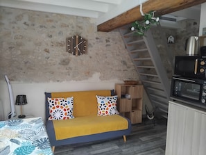 Une pièce chaleureuse avec un canapé, une étagère en bois, une horloge murale et un escalier.