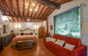 Ein Schlafzimmer mit einem Bett, einem roten Sofa, einer Holzkiste, einem Schrank aus Holz, einem Spiegel und einem Fenster mit Jalousien.