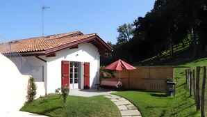 Une maison avec un toit recouvert de tuiles rouges, une façade blanche et un petit jardin avec un chemin menant à l’entrée.