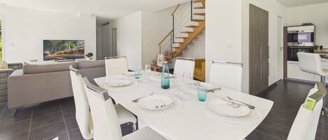 A modern dining area with a white table set for four, a staircase, and a kitchen in the background.