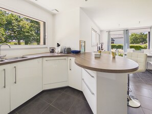 A modern kitchen with a curved island, a built-in sink, and a large window offering a view of greenery. - House near beaches for 6 with garden (Fouesnant)