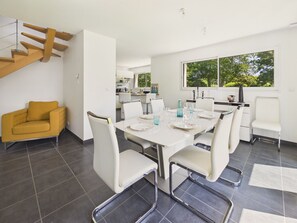 A modern dining area with a white table set for six, surrounded by white chairs, a yellow armchair, and a staircase. - House for 6 in Fouesnant with garden (Fouesnant)