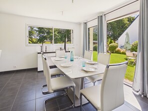 A modern dining room with a large table set for four, white chairs, and a view of a garden through large windows. - House for 6 in Fouesnant with garden (Fouesnant)