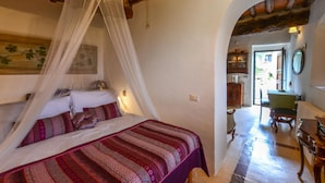 Una camera da letto con un letto, una tenda a baldacchino, un quadro, un'area pranzo con tavolo e sedie, e un arco che conduce in un'altra stanza.