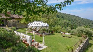 Un giardino con un gazebo, un'amaca e una casa in pietra.
