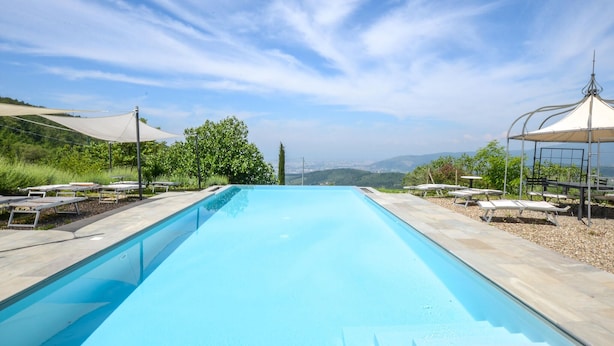 Una piscina con lettini e ombrelloni, immersa nel verde con vista su montagne lontane.