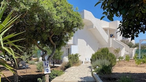 Un bâtiment blanc avec un chemin de pierre menant à une porte, entouré de verdure et sous un ciel dégagé.