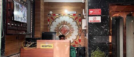 A reception area with a reception desk, a sofa, a television, a CCTV sign, and a no smoking sign.