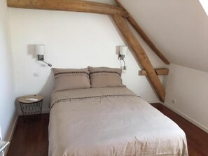 A bedroom with a bed, two wall-mounted lamps, a round nightstand, and exposed wooden beams.
