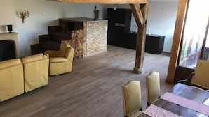 Ein geräumiger Wohnbereich mit Holzboden, einem Kamin, einer Sofagarnitur, einem Esstisch mit Stühlen und einer Küchenzeile im Hintergrund.