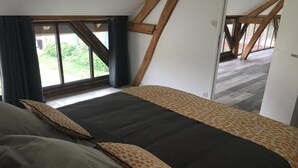 Ein Schlafzimmer mit einem großen Bett, einem Fenster mit Vorhängen und Blick ins Freie.