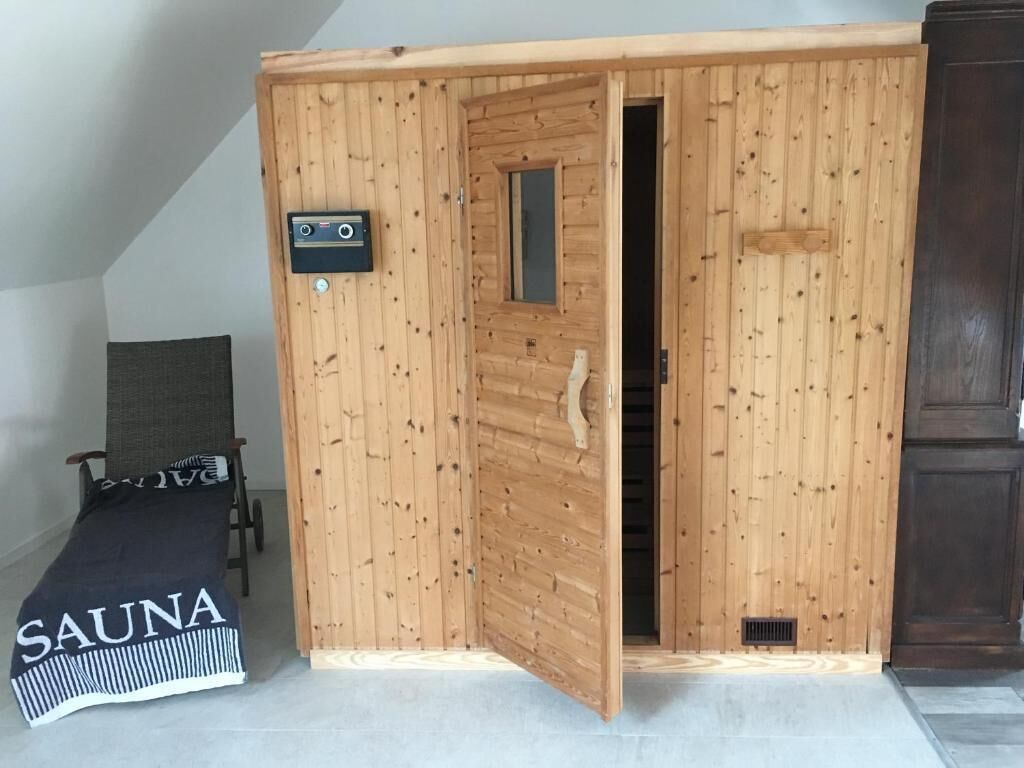 Una sala de sauna con puerta de madera, panel de control y banco con un letrero que dice 'SAUNA'.