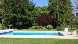 Ein rechteckiger Pool mit Rasenfläche, Bäumen und zwei weißen Liegestühlen.