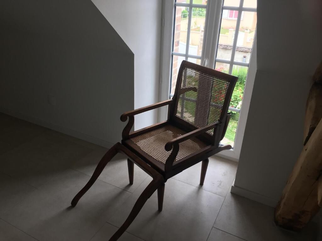 Una silla de madera con respaldo tejido en una habitación con un ventanal grande.