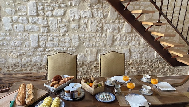Ein Frühstückstisch mit Brot, Gebäck, Früchten und Getränken vor einer Steinwand.