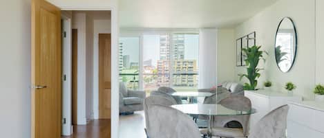 Un comedor moderno con una mesa y sillas de vidrio, un sofá y vistas a rascacielos.