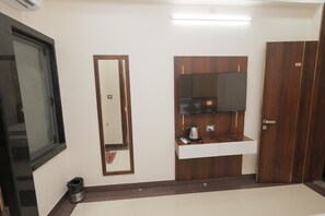 A room with a wooden wardrobe, a mirror, a white countertop with a kettle, and a trash bin. - Aora Hotels And Villas  (Udaipur)