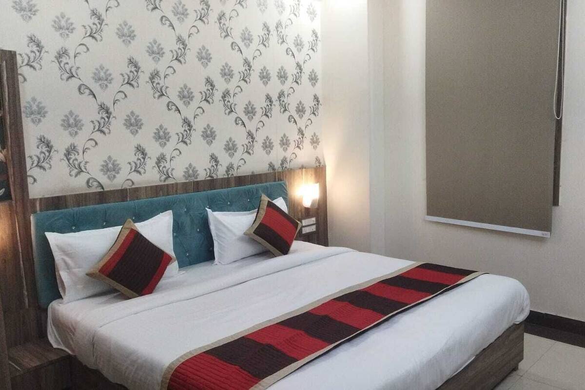 Una habitación de hotel con una cama, cabecera, luz empotrada en la pared y una ventana.