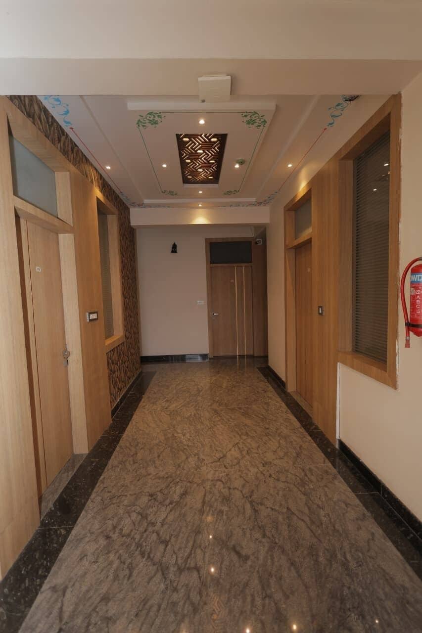 Un pasillo con puertas de madera, suelo de mármol y techo con detalles decorativos.