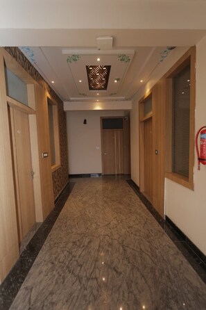 A hallway with wooden doors, a marble floor, and a ceiling with decorative patterns. - Aora Hotels And Villas  (Udaipur)