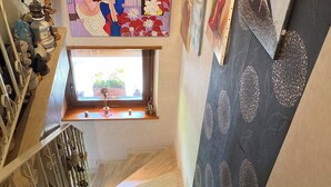 Eine Treppe mit einem Fenster am oberen Ende, eine dekorative Wand mit floralem Muster und ein Regal mit verschiedenen Gegenständen.