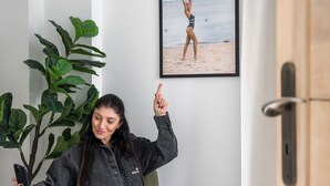 Una persona seduta su una sedia in una stanza con una pianta grande, un quadro appeso al muro e una porta in legno.