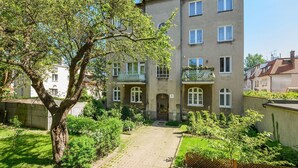 Un edificio residenziale a più piani con un cortile lastricato, un albero e un piccolo giardino.