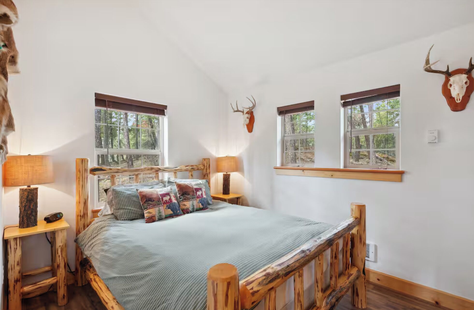 Ein Schlafzimmer mit einem Bett, zwei Nachttischen, einem Fenster und einem Hirschschädel an der Wand.