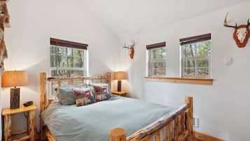 Ein Schlafzimmer mit einem Bett, zwei Nachttischen, einem Fenster und einem Hirschschädel an der Wand.