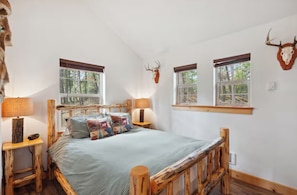 Ein Schlafzimmer mit einem Bett, zwei Nachttischen, einem Fenster und einem Hirschschädel an der Wand.
