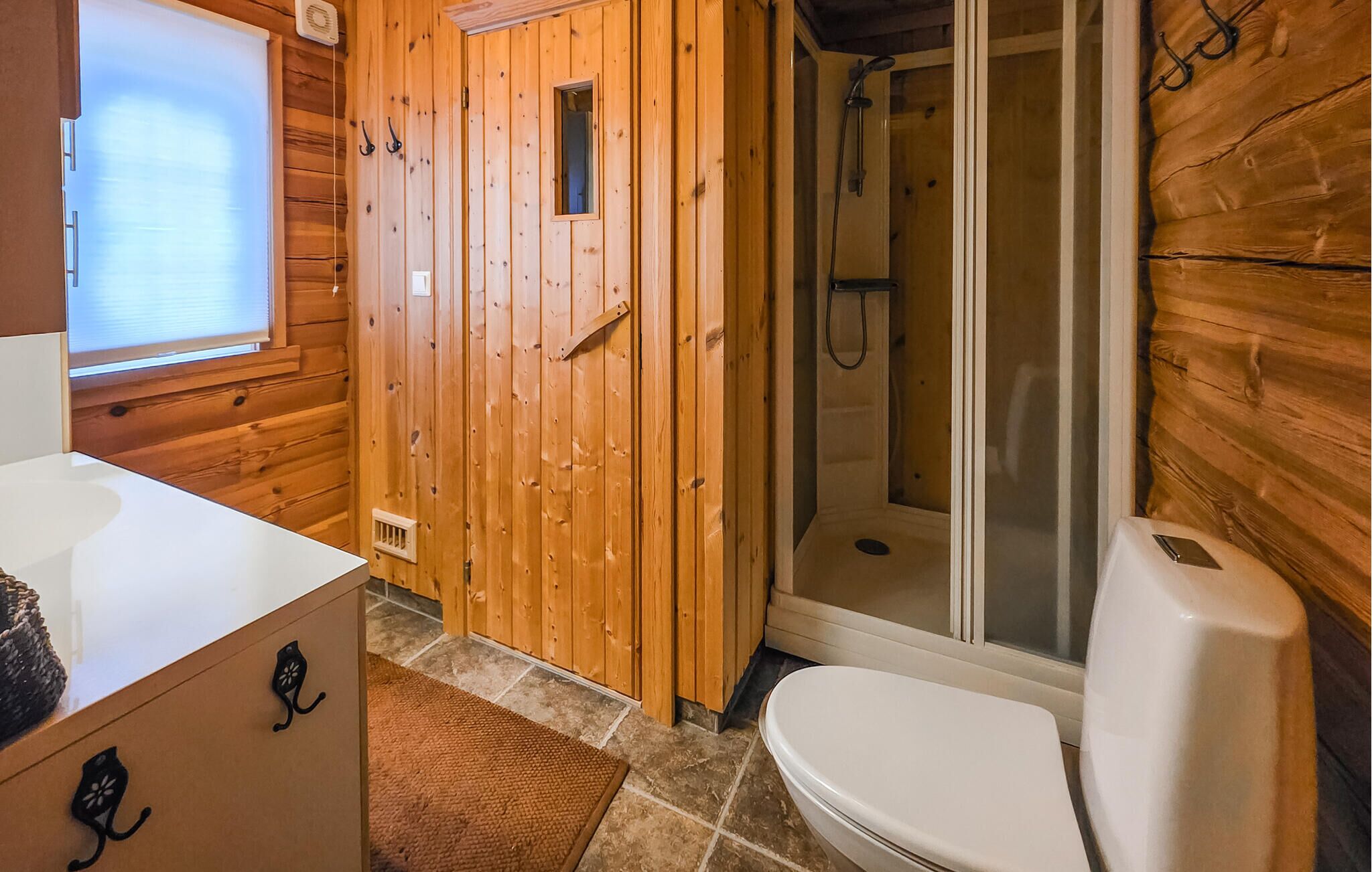Ein Badezimmer einer Holzhütte mit Dusche, Toilette und einem Fenster.