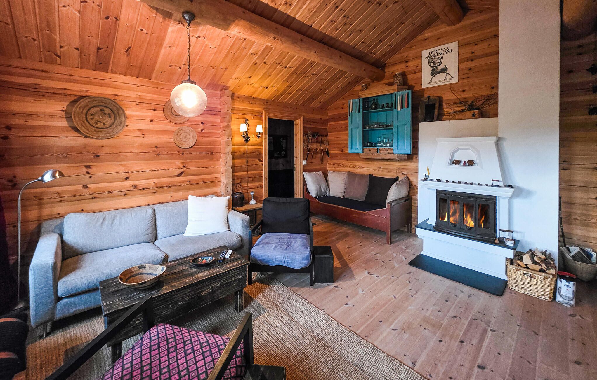 A cozy log cabin interior with a sofa, armchair, and a fireplace.