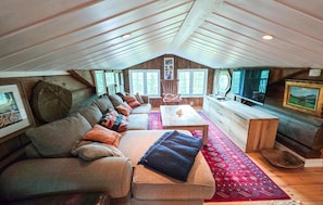 A cozy attic room with a sofa, a coffee table, a TV, and a wooden desk.