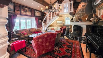 A spacious living room with a grand staircase, a fireplace, and a piano.
