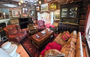 A log cabin interior with a fireplace, wooden furniture, and various framed artworks.