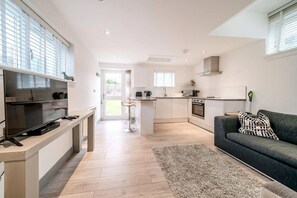 A modern kitchen with a TV, bar stools, and a dining area. - The Wee House | Elie (Elie)