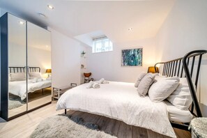 Un dormitorio con cama, espejo, ventana y un cuadro en la pared.