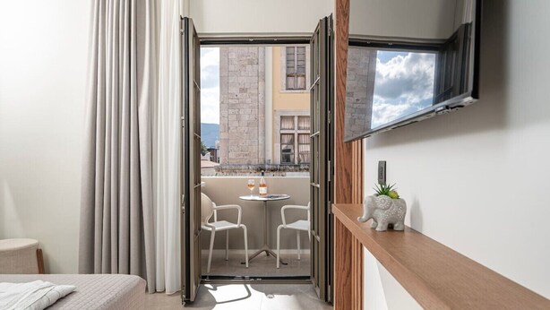 Ein modernes Hotelzimmer mit Balkon, einem Bett, einem Fernseher und einem kleinen Tisch mit Stühlen.