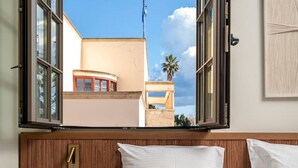 Ein Hotelzimmer mit großem Fenster, einem Bett mit weißer Bettwäsche, einem Nachttisch aus Holz und einem Bademantel auf dem Bett.
