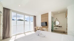 Una habitación de hotel con una cama grande, un escritorio con sillas, un televisor, un baño con espejo y vistas al mar.