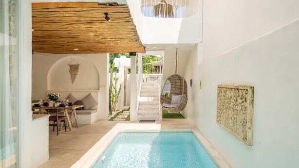 Un interior moderno con piscina, una silla colgante y una escalera que da al exterior.