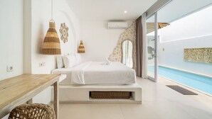 Un dormitorio con cama, una mesita, muebles de mimbre, aire acondicionado instalado en la pared y vista a una piscina.