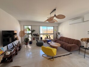 A living room with a sofa, a yellow chair, a TV, and a ceiling fan. - Large apartment in the heart of the 7th district - 5min from the old port (Marseille)