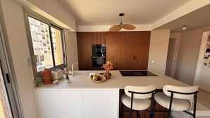 Ett modernt kök med en central köksö, barstolar, en inbyggd ugn och ett fönster med utsikt över ett bostadsområde.