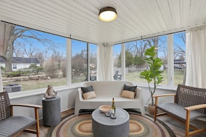 A sunroom with a white sofa, two chairs, a round coffee table, a potted plant, and a view of the outside. - NEW! Designer Home - King Beds, Glass Sunroom, Game Room, BBQ (Southfield)