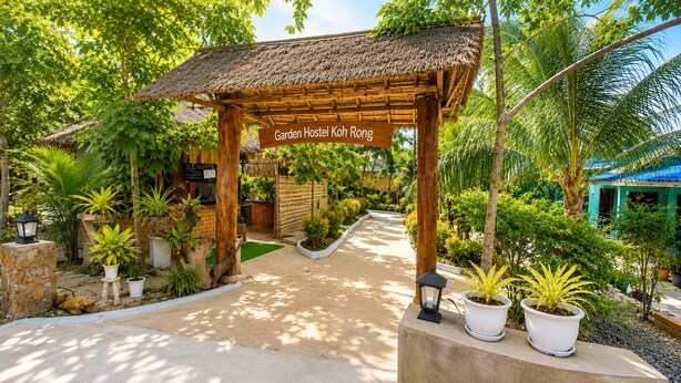 Una pérgola de madera con un letrero que dice 'Garden Hostel Koh Rong' y un sendero que conduce a un edificio.