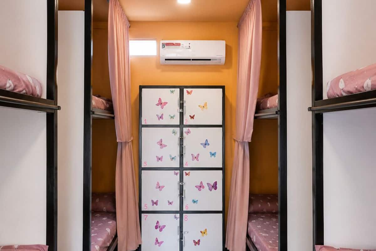 Dormitorio con literas, ventilador de techo, unidad de aire acondicionado y pared con cajas de almacenamiento numeradas.