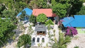 Un resort con varias construcciones, una estructura central con techo oscuro y abundante vegetación alrededor.