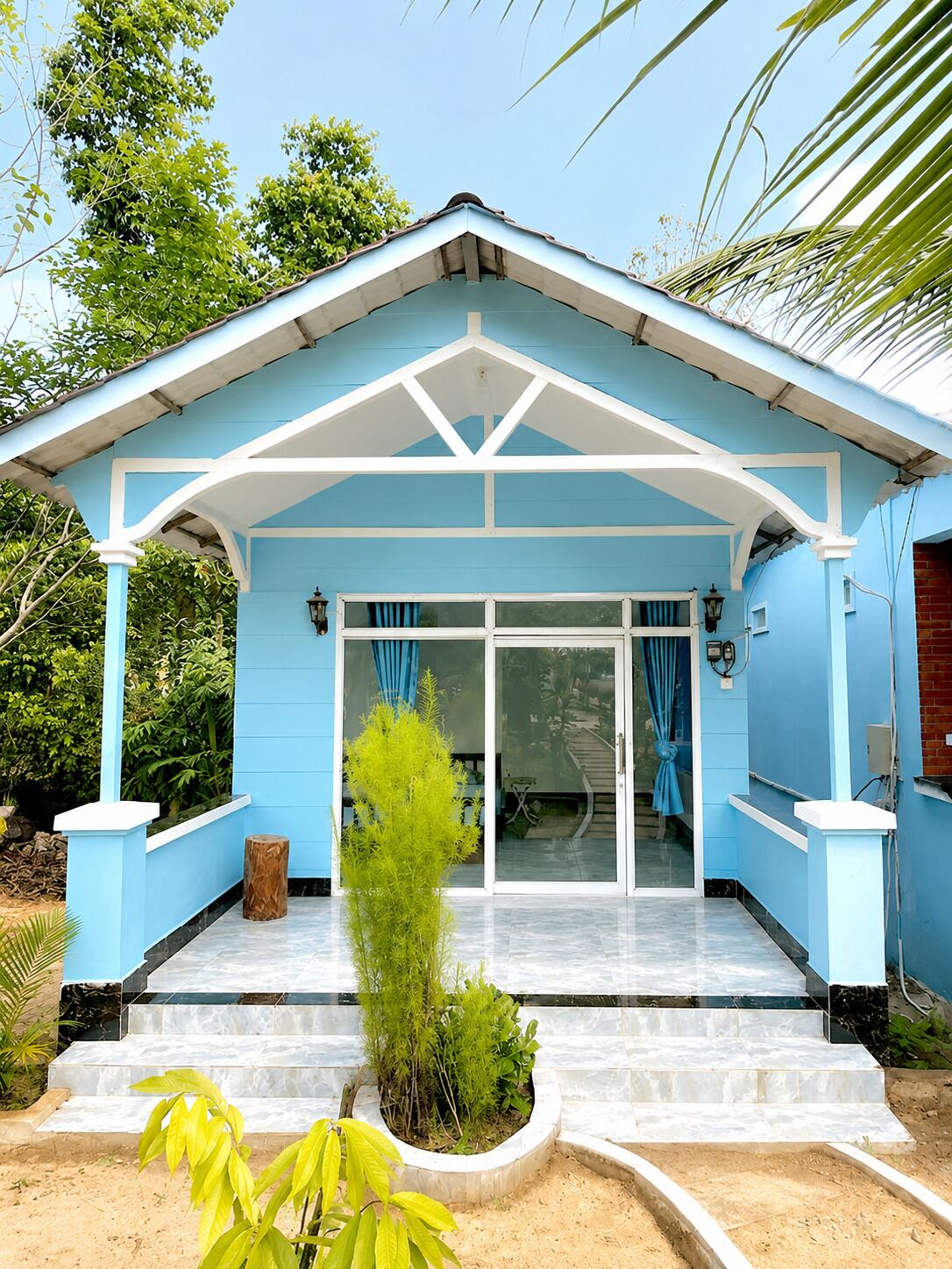 A blue building with a covered entrance, a small garden, and a clear sky.